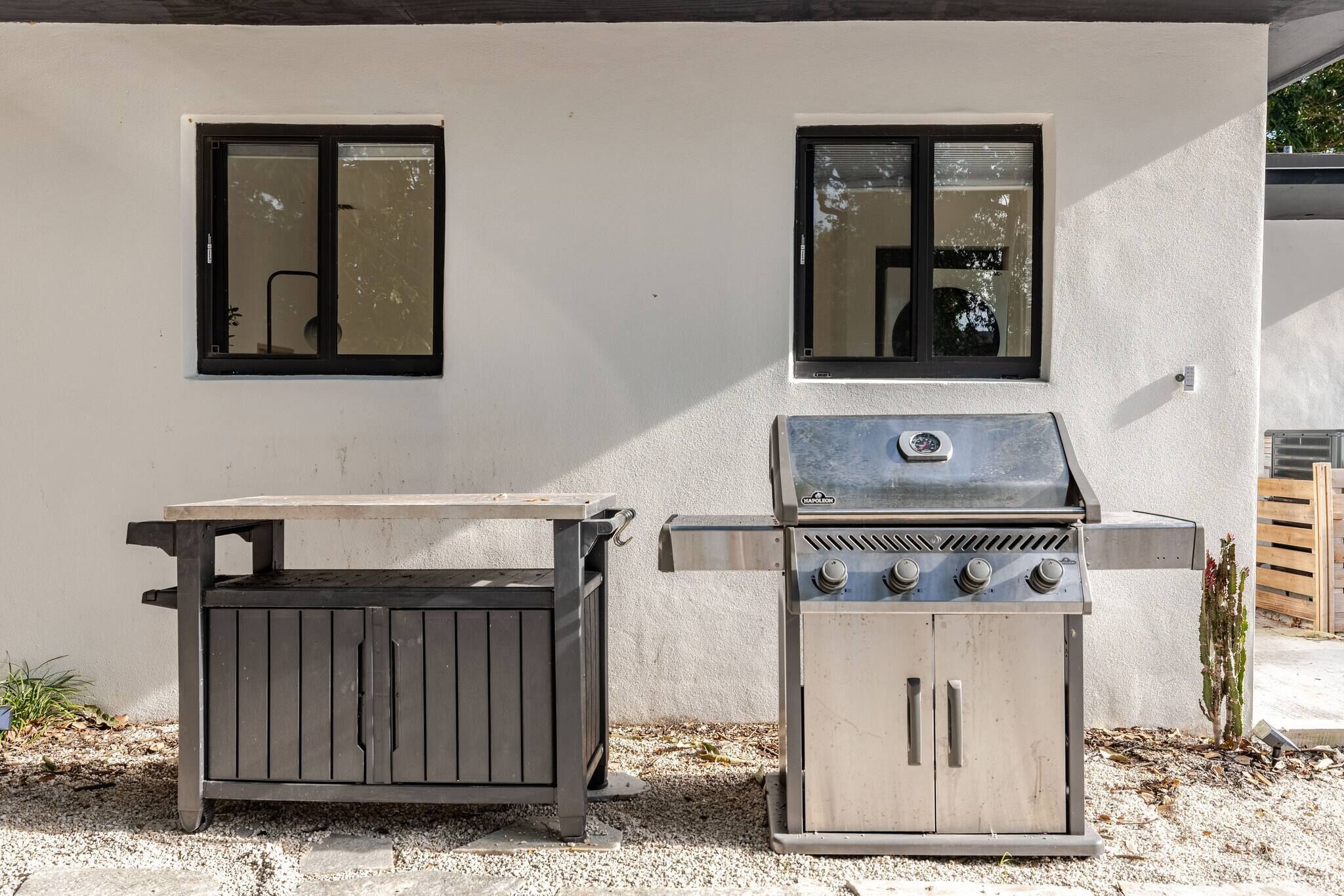 Een buitenbarbecue en een houten tafel voor een gebouw met twee ramen.