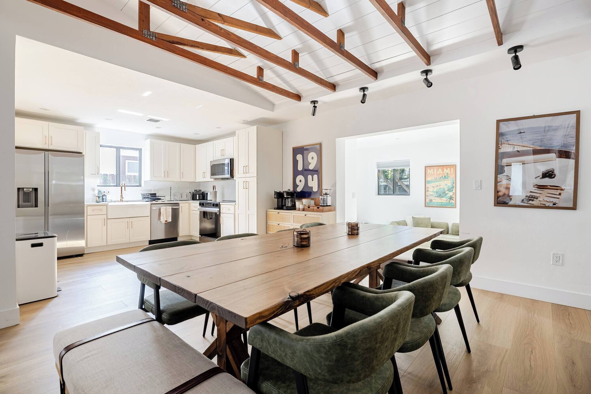 Una cocina moderna con electrodomésticos de acero inoxidable, un comedor con mesa de madera y sillas verdes, y vistas al exterior.