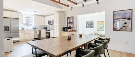 Una cocina moderna con electrodomésticos de acero inoxidable, un comedor con mesa de madera y sillas verdes, y vistas al exterior.