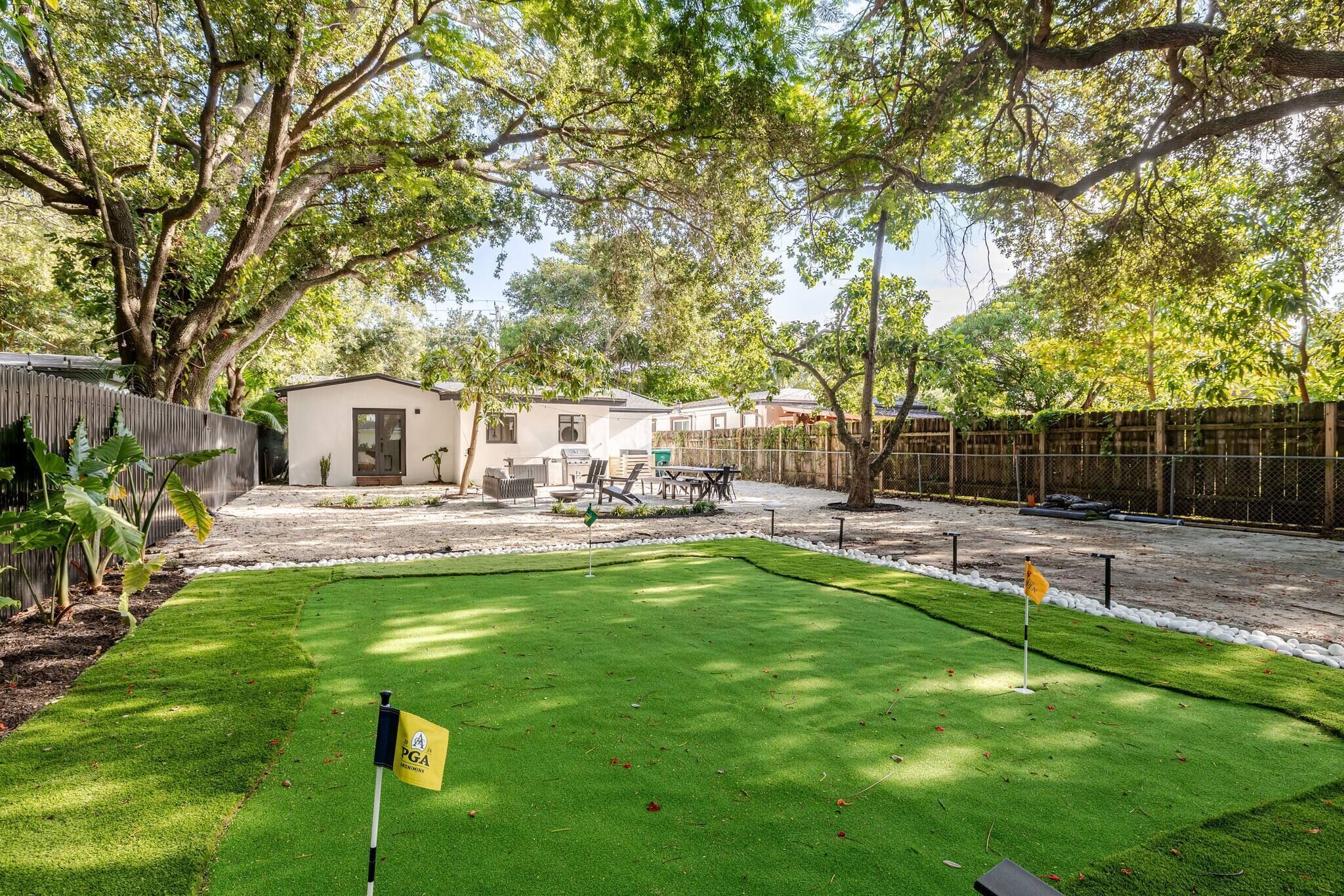 Zona residencial con césped cuidado, una bandera de golf y una casa con patio cercado.