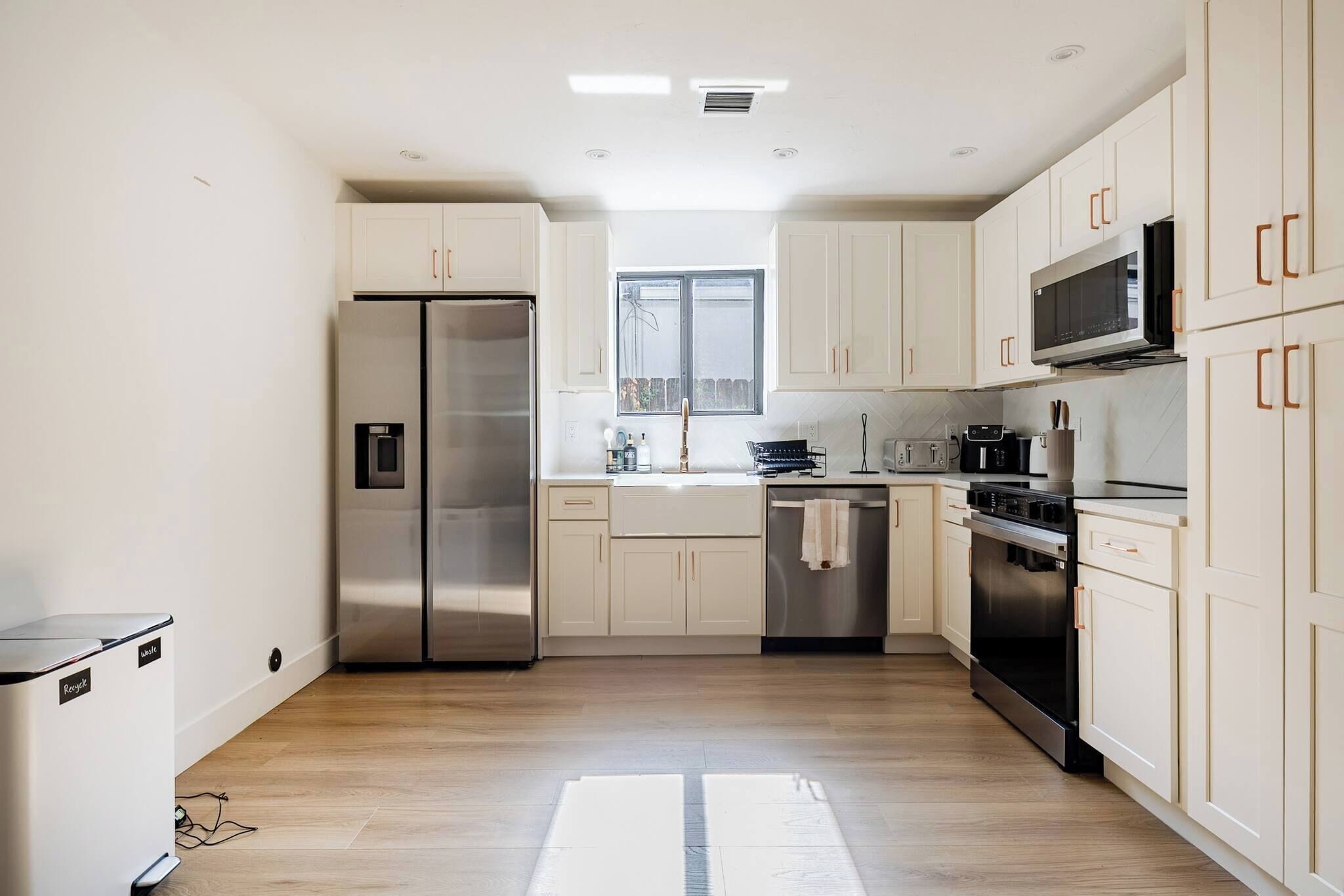 A modern kitchen with stainless steel appliances, white cabinetry, and a window providing natural light.