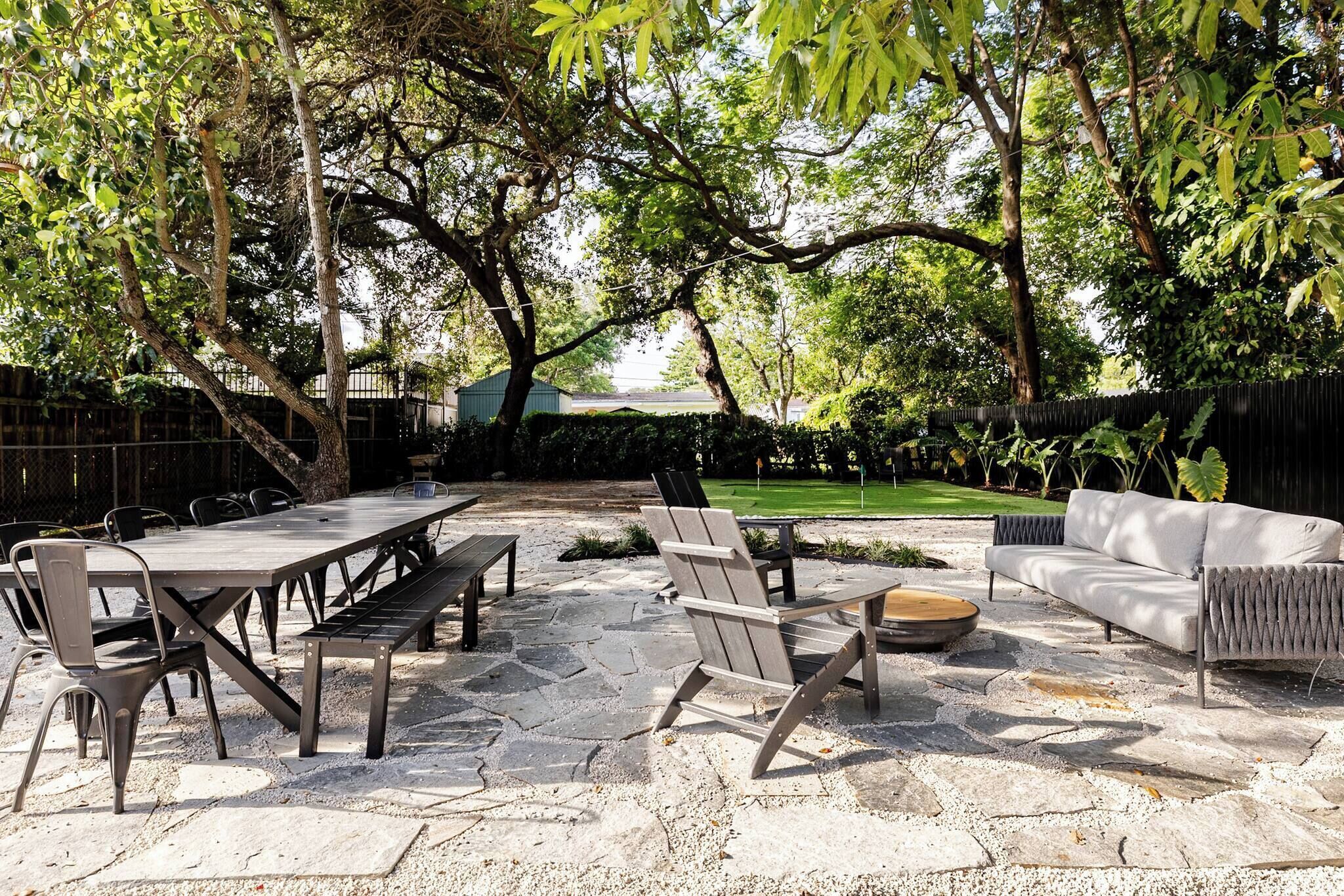 An outdoor patio with stone flooring, a dining table, chairs, a sofa, and a fire pit.