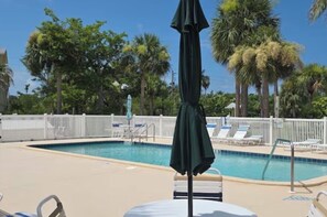 A swimming pool with lounge chairs and umbrellas, surrounded by palm trees and a white fence. - Don’t Worry- Beach Happy!  Little Gasparilla Island (Placida)