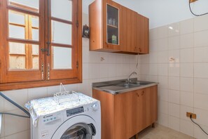 A compact kitchen with wooden cabinets, a built-in sink, and a front-loading washing machine. - Apartment 'Casa Lucia appartamento vacanze' with Sea View, Wi-Fi and Air Conditioning (Avola)