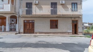 A two-story building with a balcony, a garage door, and a street in front. - Apartment Lucia with Sea View, Wi-Fi, and Air Conditioning (Avola)