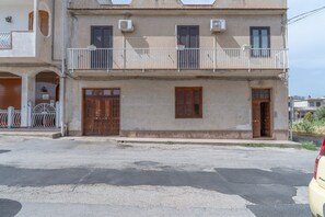 Ein zweistöckiges Gebäude mit Balkon, einer Garagenöffnung und einer Straße davor.