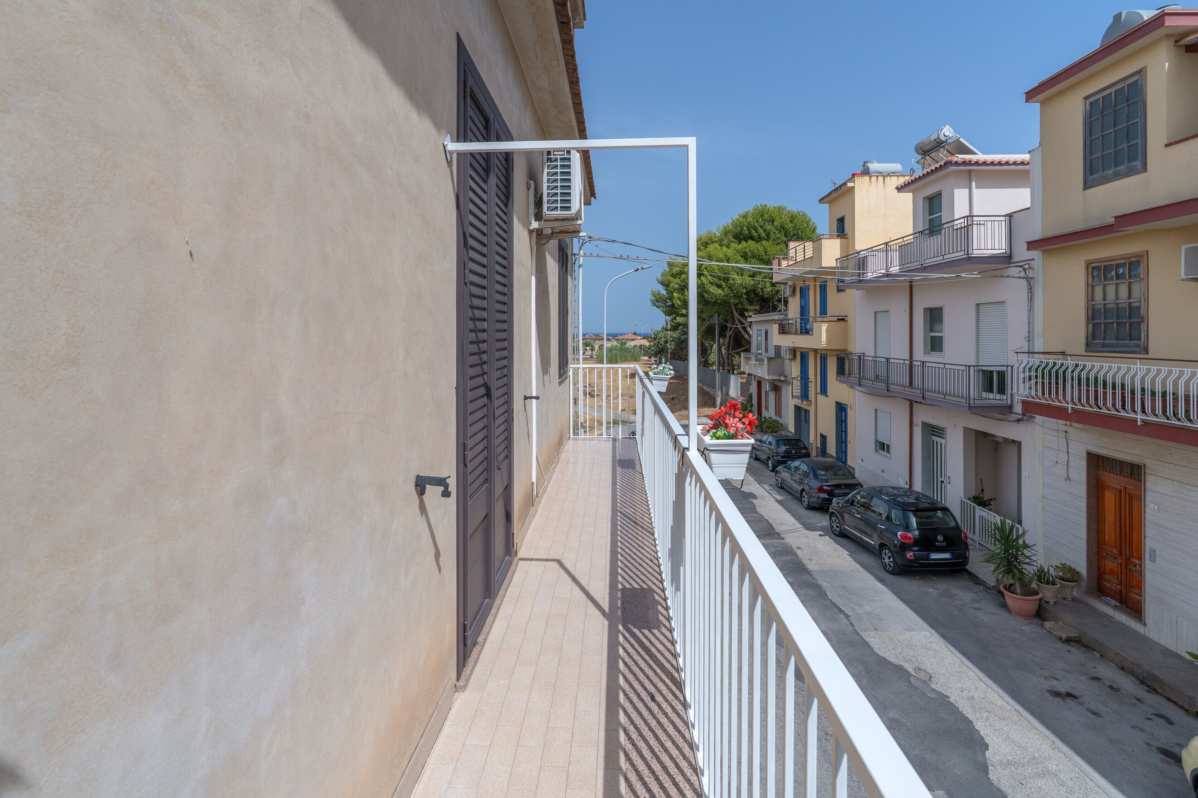 Eine enge Straße mit Gebäuden an beiden Seiten, ein Balkon mit weißer Reling und ein klarer Himmel.