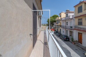 A narrow street with buildings on both sides, a balcony with a white railing, and a clear sky. - Apartment 'Casa Lucia appartamento vacanze' with Sea View, Wi-Fi and Air Conditioning (Avola)