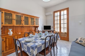 A dining area with a table set for four, wooden cabinets, a television, and a large window. - Apartment 'Casa Lucia appartamento vacanze' with Sea View, Wi-Fi and Air Conditioning (Avola)