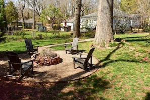 Ein Garten mit Feuerstelle, Sitzgelegenheit und einem großen Baum.