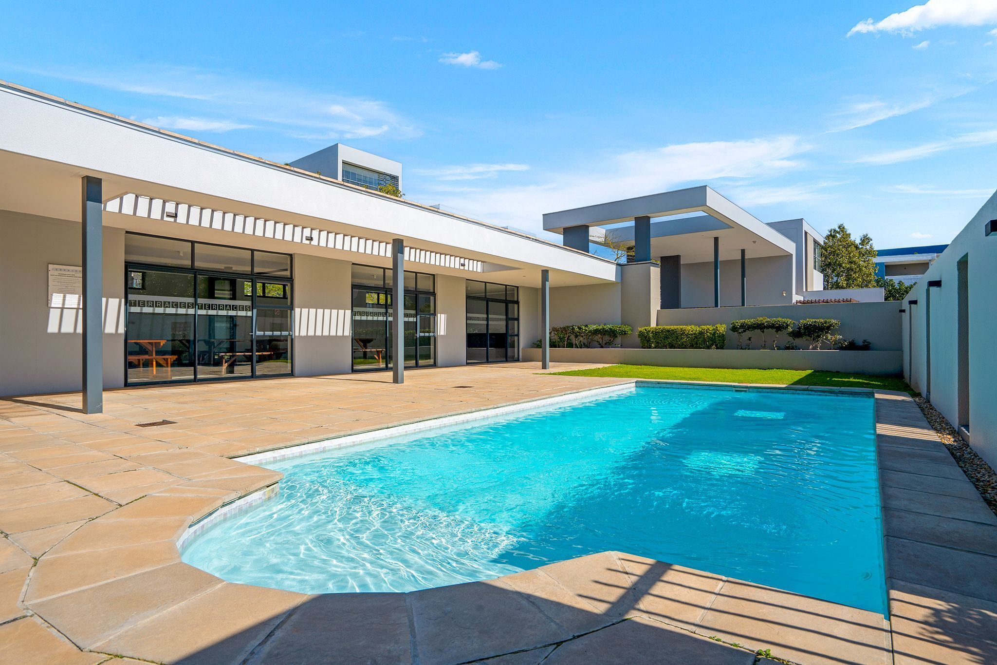 A modern outdoor swimming pool with a clear blue water surface, surrounded by a patio area with stone tiles.