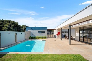 A modern outdoor swimming pool with a clear blue water surface, surrounded by a paved patio area with a grassy foreground. - The Terraces 220 - Two Bedroom Apartment, Sleeps 4 (Cape Town)
