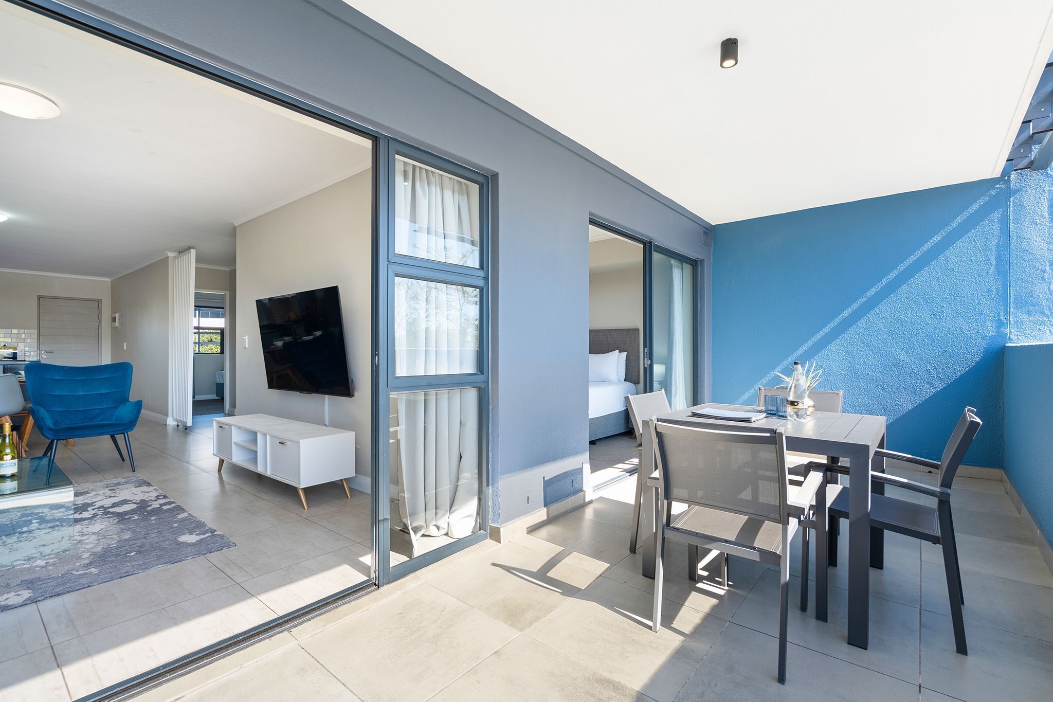 A modern living space with a dining area, a TV mounted on the wall, and a large sliding glass door leading to an outdoor area.