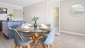 A modern kitchen with a dining area, featuring a glass table, grey chairs, and a white partition. - The Terraces 220 - Two Bedroom Apartment, Sleeps 4 (Cape Town)