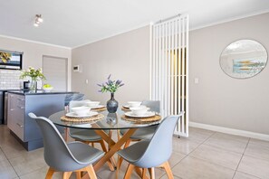 A modern kitchen with a dining area, featuring a glass table, grey chairs, and a white partition. - The Terraces 220 - Two Bedroom Apartment, Sleeps 4 (Cape Town)