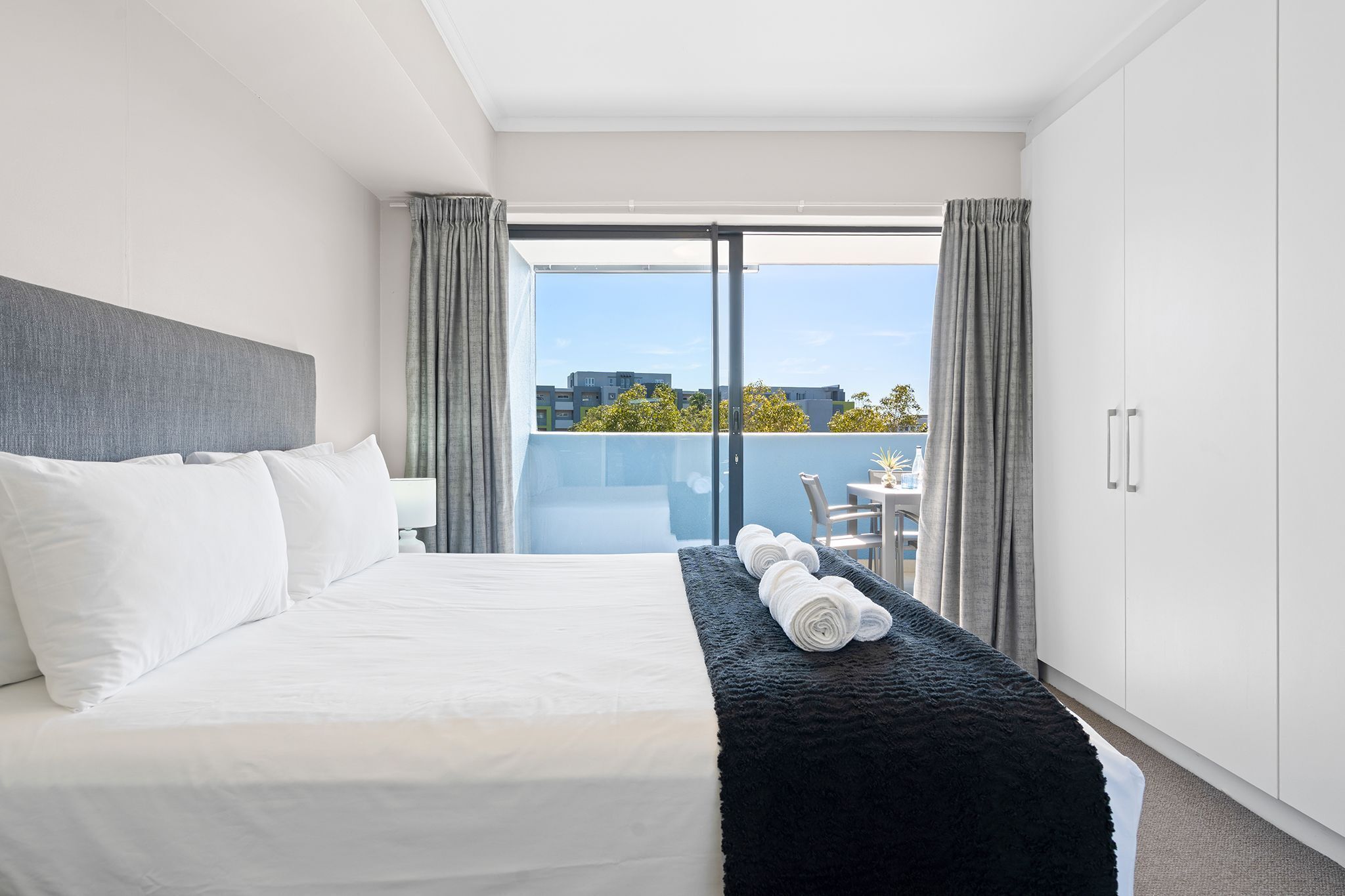 A modern hotel room with a large bed, a balcony, and a view of the city.