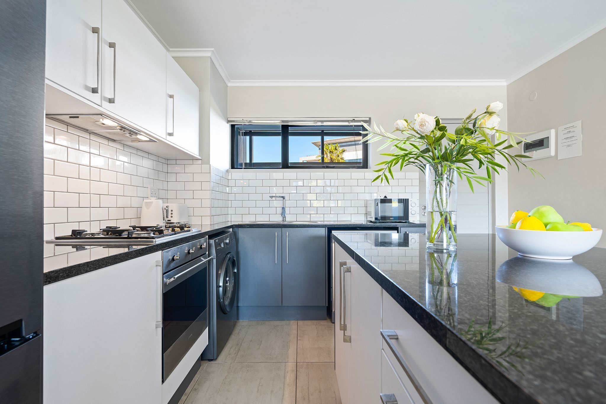 A modern kitchen with white cabinetry, a black countertop, and a window above the sink.