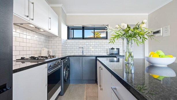 A modern kitchen with white cabinetry, a black countertop, and a window above the sink. - The Terraces 220 - Two Bedroom Apartment, Sleeps 4 (Cape Town)