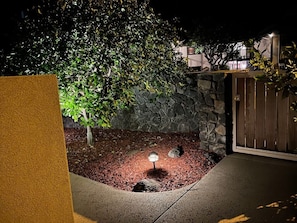 A landscaped garden area with a stone wall, a wooden gate, and a well-lit pathway. - Steps to Maui's Charley Young Beach Condo Apt 1 (Kihei)