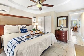 Habitación de hotel con cama, cómoda, ventilador de techo y vista al pasillo.