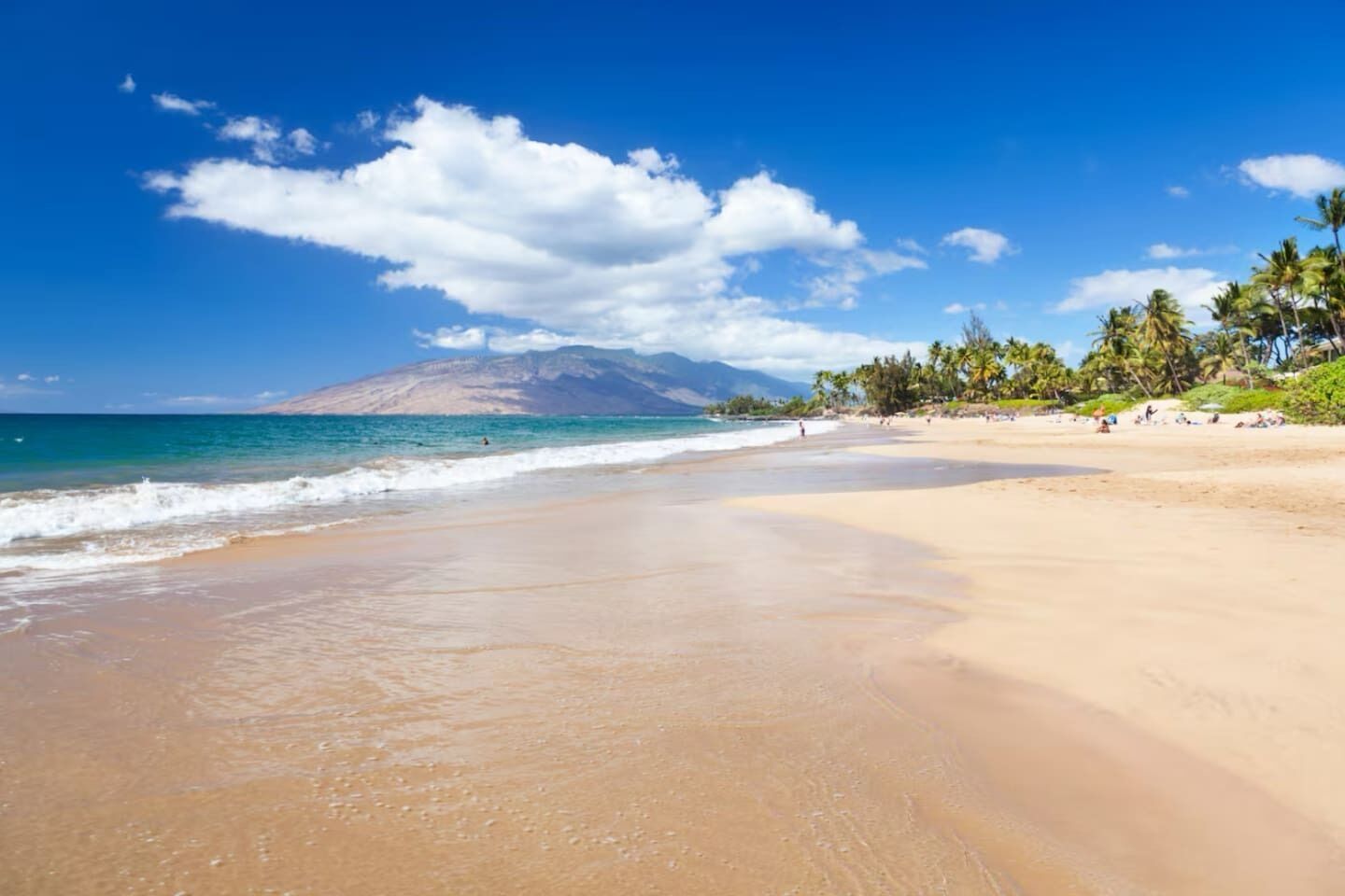 A beach with a clear sky, calm sea, and a mountain in the background.