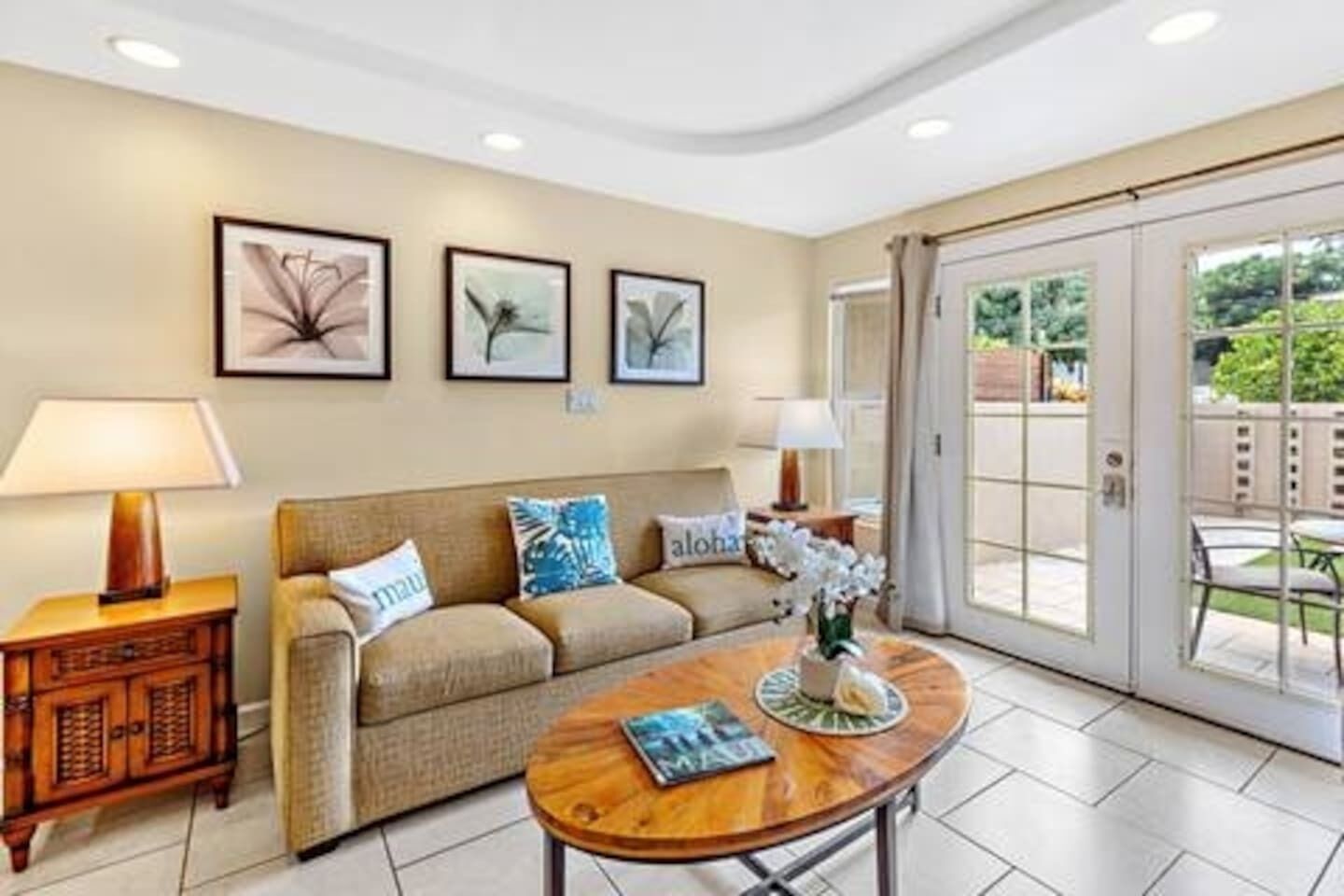 A living room with a sofa, coffee table, and lamps. There are framed pictures on the wall and a sliding glass door leading to an outdoor area.