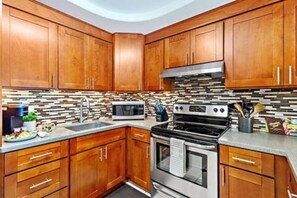 Una cocina con gabinetes de madera, estufa de acero inoxidable, microondas y salpicadero de azulejos.