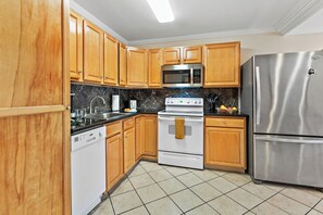 Eine Küche mit Holzschränken, einem Edelstahl-Kühlschrank, einer Mikrowelle, einem Backofen und einem Geschirrspüler.