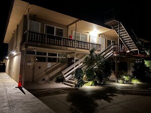 A multi-story building with a staircase leading to a balcony, a garage, and potted plants. - Steps to Maui's Charley Young Beach Condo Apt 6 (Kihei)