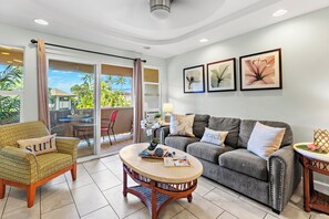 A living room with a sofa, armchair, and coffee table, a balcony with a view, and three framed pictures on the wall. - Steps to Maui's Charley Young Beach Condo Apt 6 (Kihei)