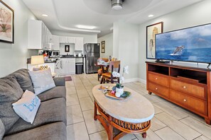 A modern living room with a sofa, a coffee table, and a television displaying a scenic ocean view. - Steps to Maui's Charley Young Beach Condo Apt 6 (Kihei)
