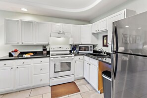 A modern kitchen with white cabinetry, stainless steel appliances, and a black countertop. - Steps to Maui's Charley Young Beach Condo Apt 6 (Kihei)