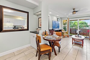 Uma cozinha moderna com armários brancos, uma área de refeições com mesa redonda e vista para o exterior através de uma porta de vidro.