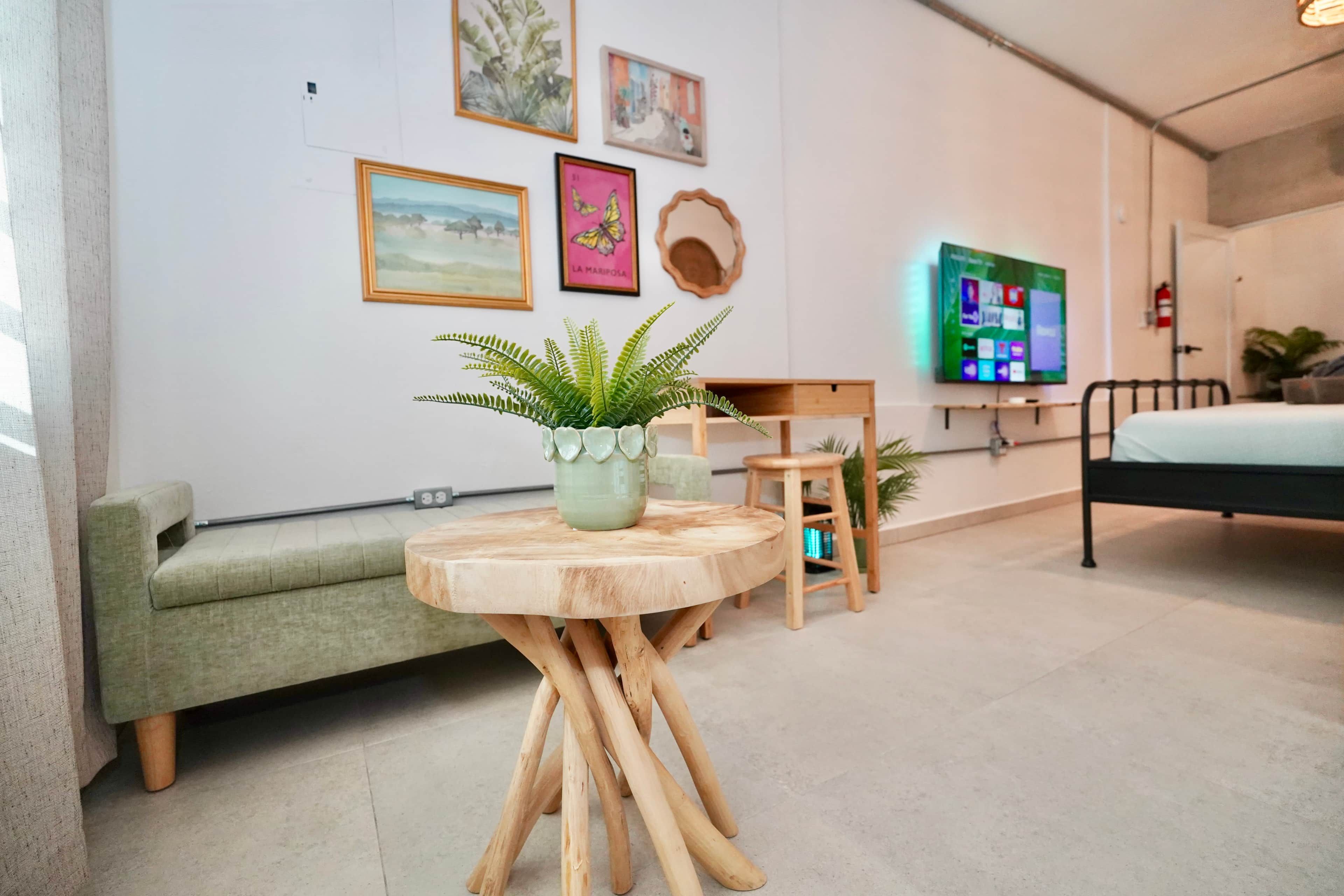 Habitación moderna con un sofá verde, una mesa redonda de madera con una planta, un televisor en la pared y una cama.
