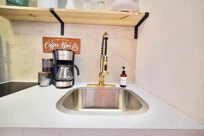 Eine Küche mit Spüle aus Edelstahl, einer Kaffeemaschine, einem Seifenspender und einem Regal mit einem Schild für Kaffee.