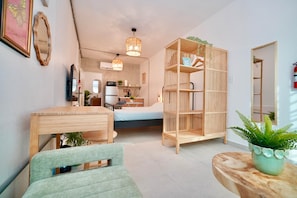 Un espacio habitable compacto con cama, mesa de comedor, estantería y pequeña cocina.