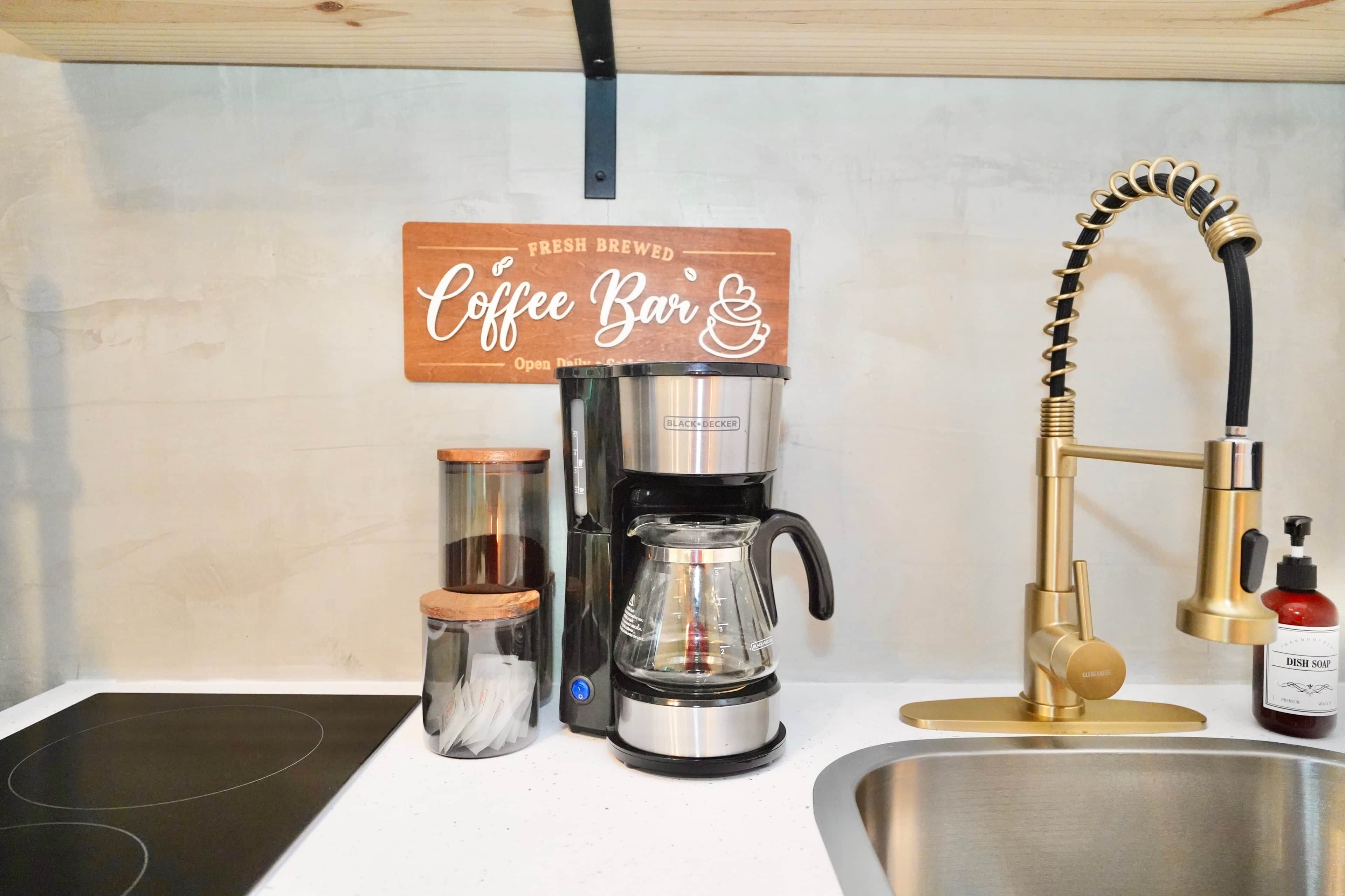 Una cocina con cafetera, un lavamanos y un grifo.
