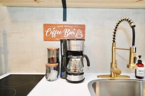 Una cocina con cafetera, un lavamanos y un grifo.
