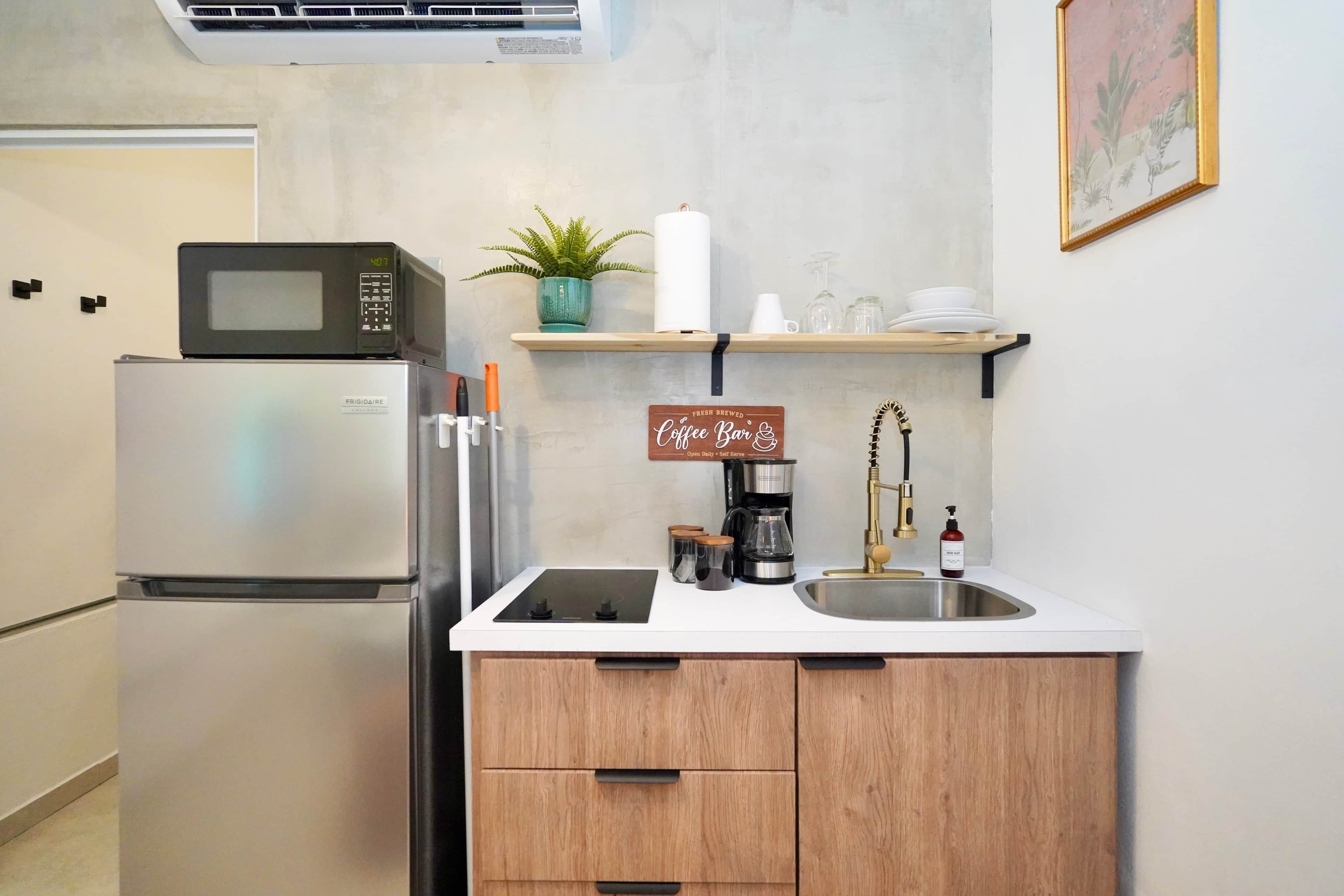 Cocina compacta equipada con refrigerador, microondas, estufa y estación de café.