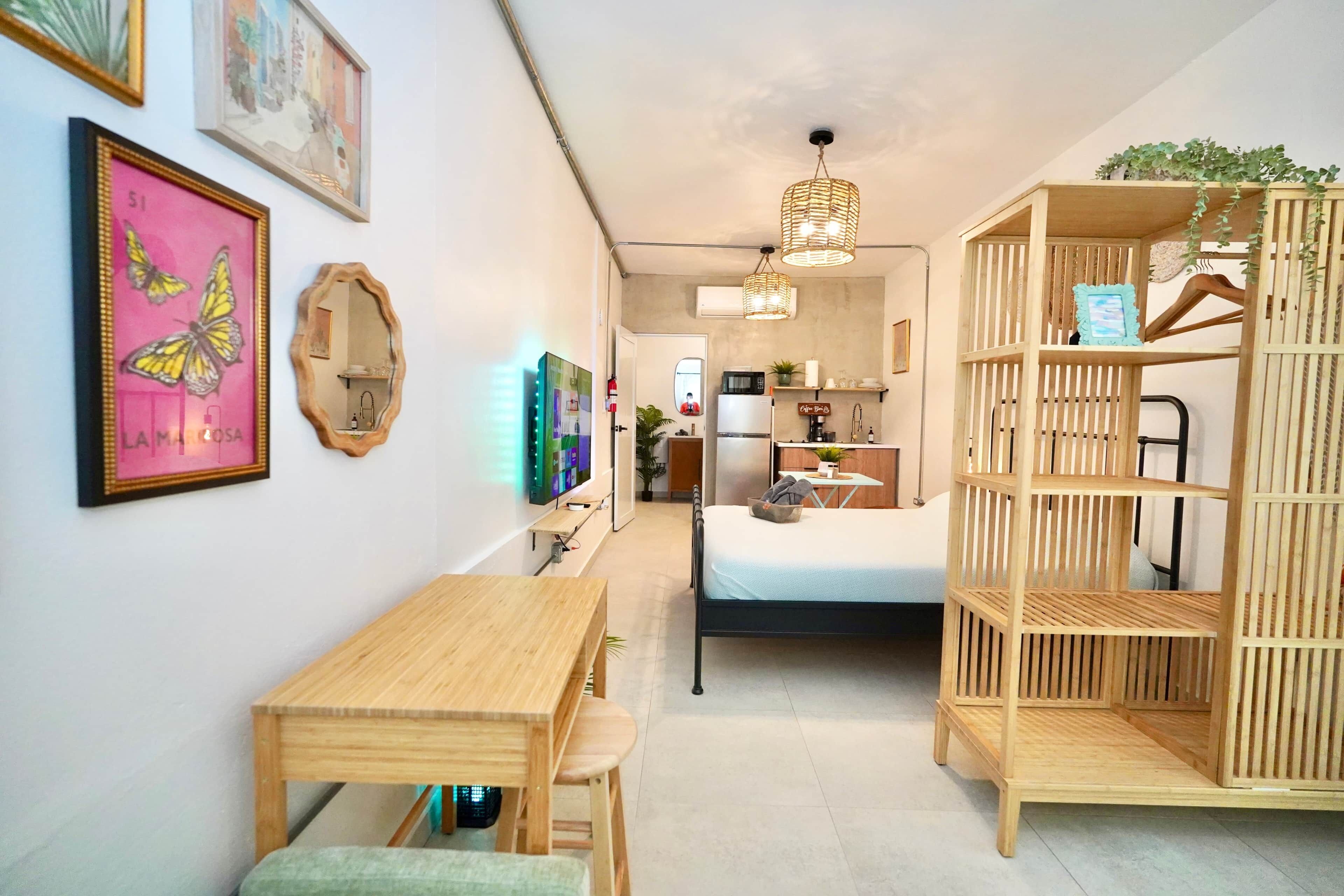 Ein gemütlicher, kompakter Wohnraum mit Bett, Holzschreibtisch, Tisch und Regalelement.