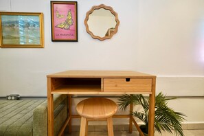 A wooden desk with a drawer, a mirror, and two framed artworks on the wall.