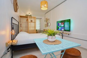 Ein Schlafzimmer mit Bett, Nachttischlampe, einem Tisch mit Pflanze, einem Fernseher an der Wand und einem Kleiderschrank.