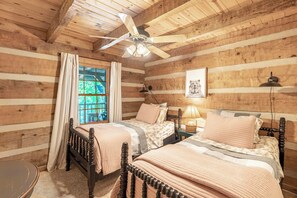 A cabin-style bedroom with two beds, a ceiling fan, a window with curtains, and a framed picture on the wall. - Tucked Away- Cabin, Pet Friendly, Hot Tub, Wood Fireplace. Fire-pit, Covered Por (Boone)