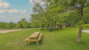 A picnic area with wooden benches and picnic tables, surrounded by trees and a small shelter. - Pocono Lake Escape | Hot Tub, Games & Outdoor Fun (Monroe County)