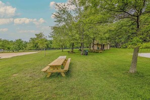 A picnic area with wooden benches and picnic tables, surrounded by trees and a small shelter. - Pocono Lake Escape | Hot Tub, Games & Outdoor Fun (Monroe County)