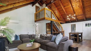 A spacious living area with a wooden ceiling, a large sofa, a coffee table, and a staircase leading to an upper level. - Pocono Lake Escape | Hot Tub, Games & Outdoor Fun (Monroe County)