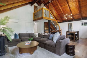 A spacious living area with a wooden ceiling, a large sofa, a coffee table, and a staircase leading to an upper level. - Pocono Lake Escape | Hot Tub, Games & Outdoor Fun (Monroe County)