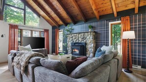 A cozy living room with a stone fireplace, wooden ceiling beams, and a large window. - Pocono Lake Escape | Hot Tub, Games & Outdoor Fun (Monroe County)