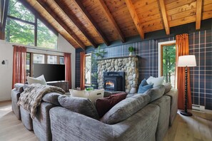 A cozy living room with a stone fireplace, wooden ceiling beams, and a large window. - Pocono Lake Escape | Hot Tub, Games & Outdoor Fun (Monroe County)