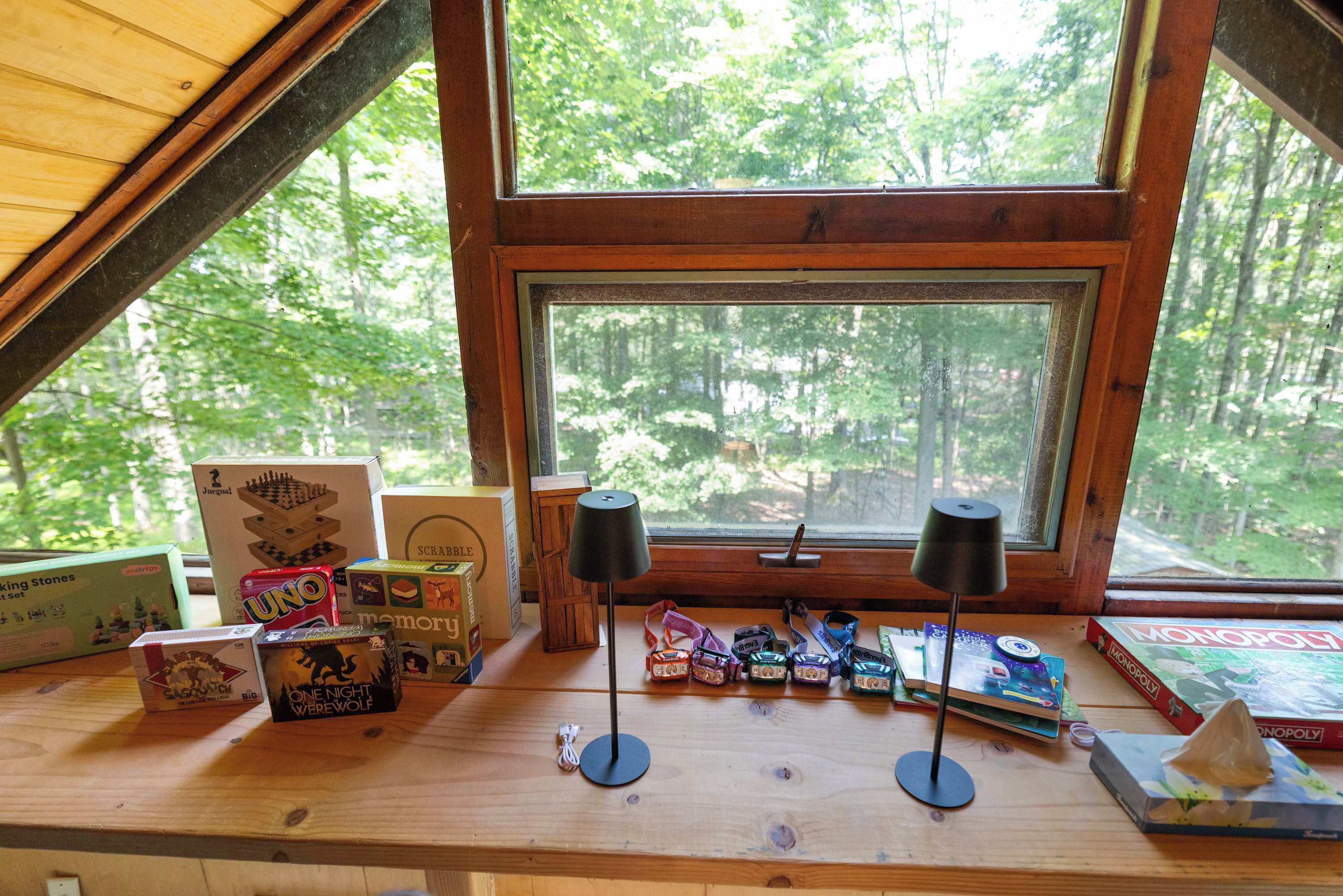 A wooden table with various board games and a window with a view of a forest.